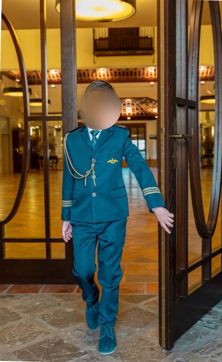 Niño con traje de comunión azul y dorado saliendo por una puerta de madera