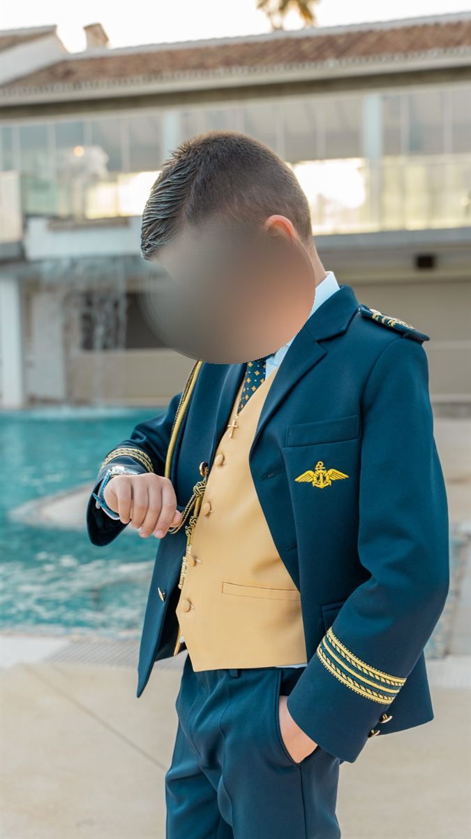 Niño de comunión mirando su reloj junto a una piscina